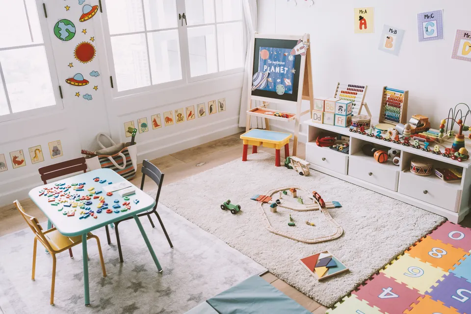 A bright classroom with a play rug, low shelves and a child-sized table