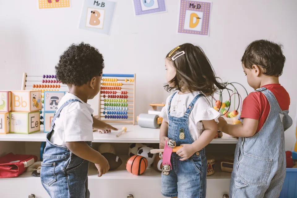 Toddlers playing together at a low shelf of toys